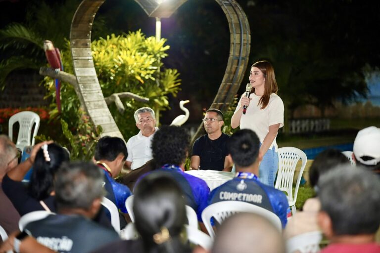 Aryel Almeida ao microfone, em pé, falando para uma plateia sentada em reunião noturna